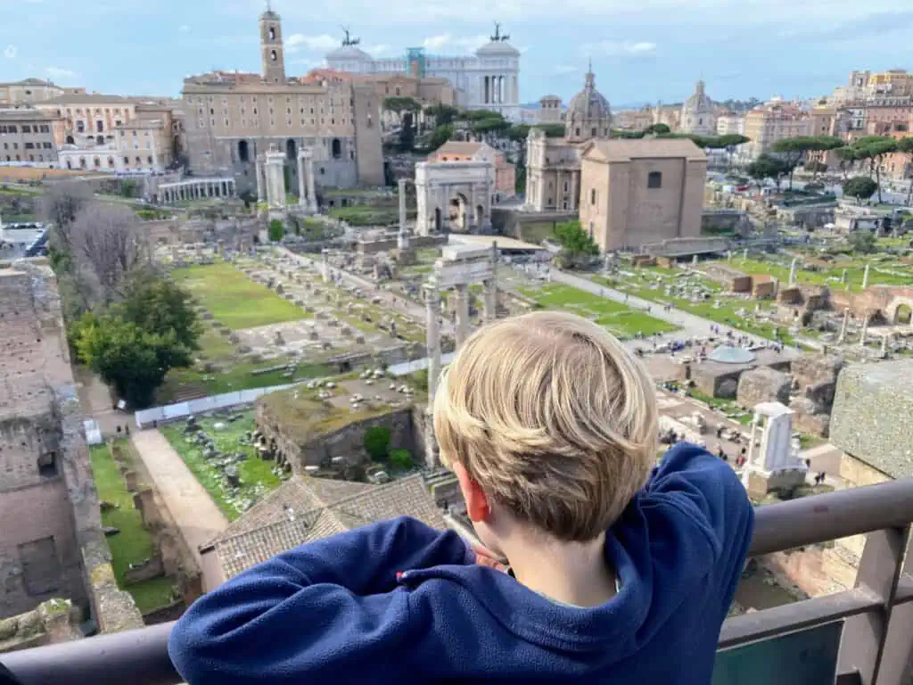 Boy looking out at Roman Forum. You can also see city skyline of Rome.