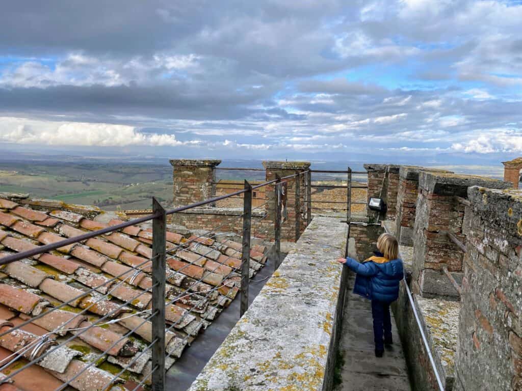 Boy walking along top of fortress walls and looking out at green rolling hills in countryside. Sunny day with clouds.