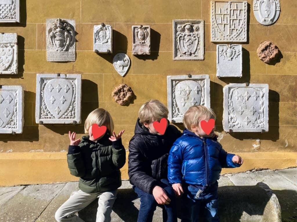 Three boys sitting in front of yellow wall with stone family crests.