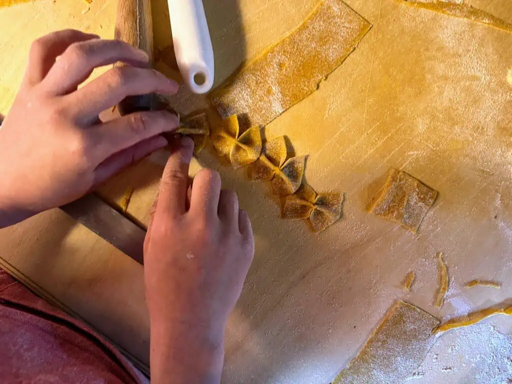 Child's hands work on shaping pasta on a wooden cutting board.