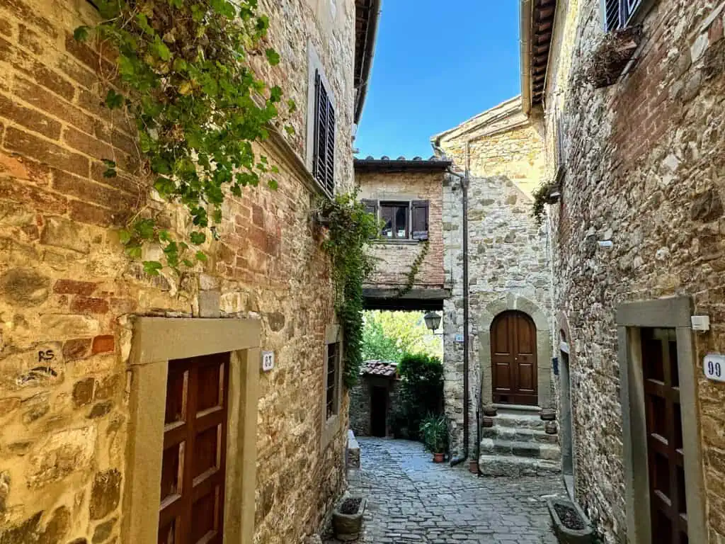 View of a small sidestreet in Montefioralle, Tuscany. Brick walls, small bridge that's part of a house in the background.