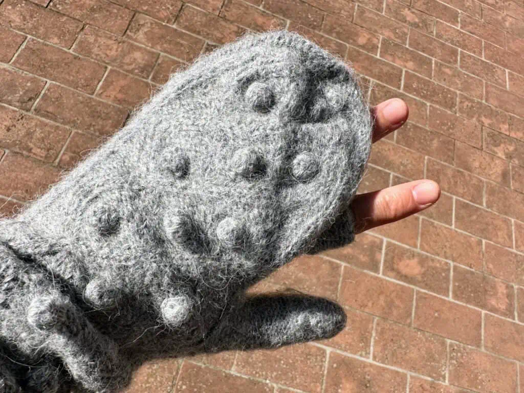 Close up of wool mitten with two fingers sticking out.