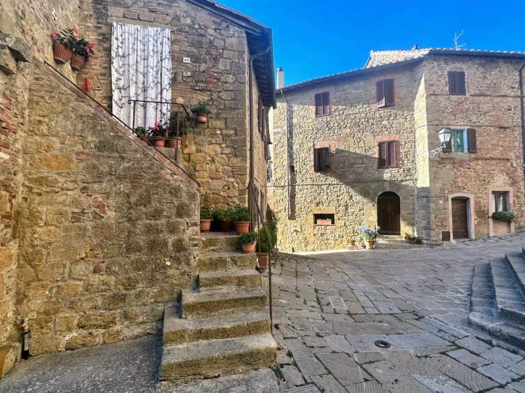 Small piazza with stone buildings. Flower pots decorate the steps and walls.