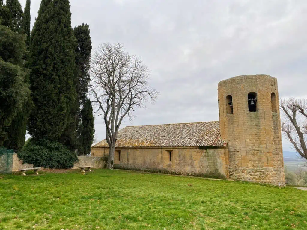 View of grassy area with cypress trees and a stone church with a round bell tower.