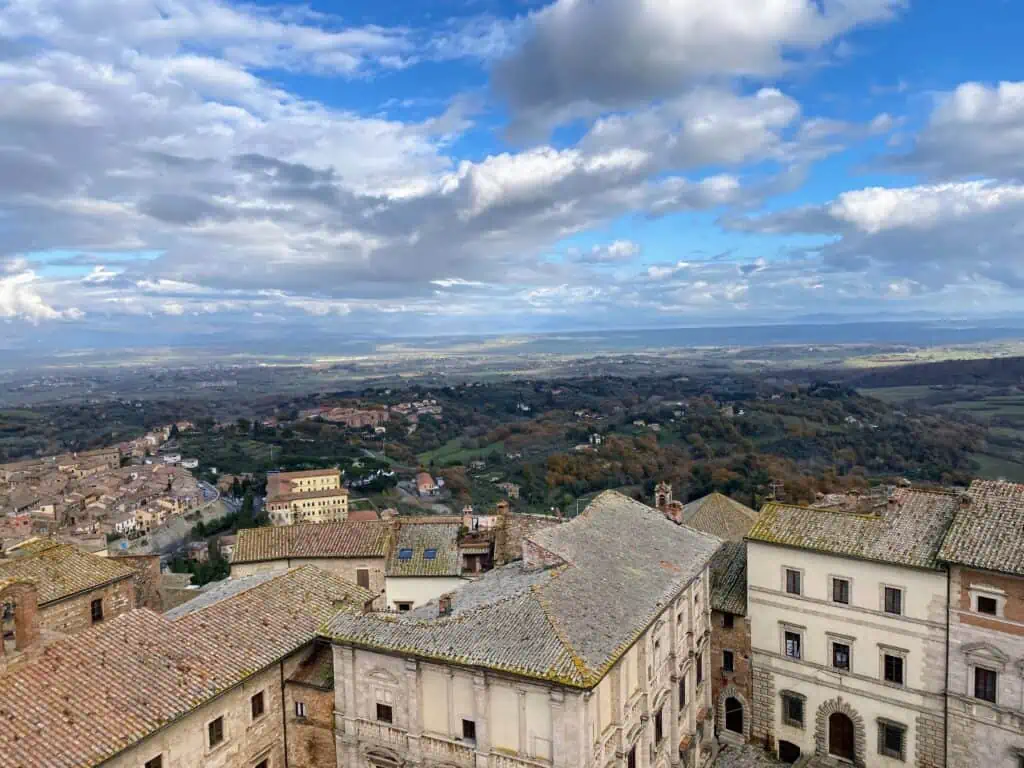 View of Tuscan countryside and the roofs and upper stories of buildings in the town of Montepulciano.