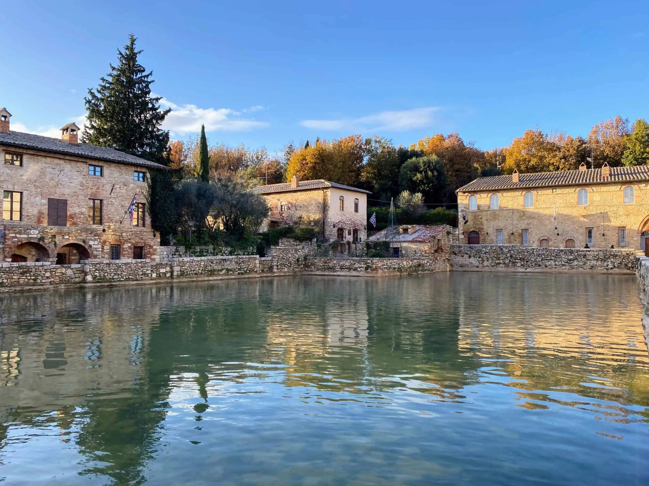 Main piazza (thermal pool) in Bagno Vignoni. It's surrounded by small stone wall and Tuscan stone buildings.