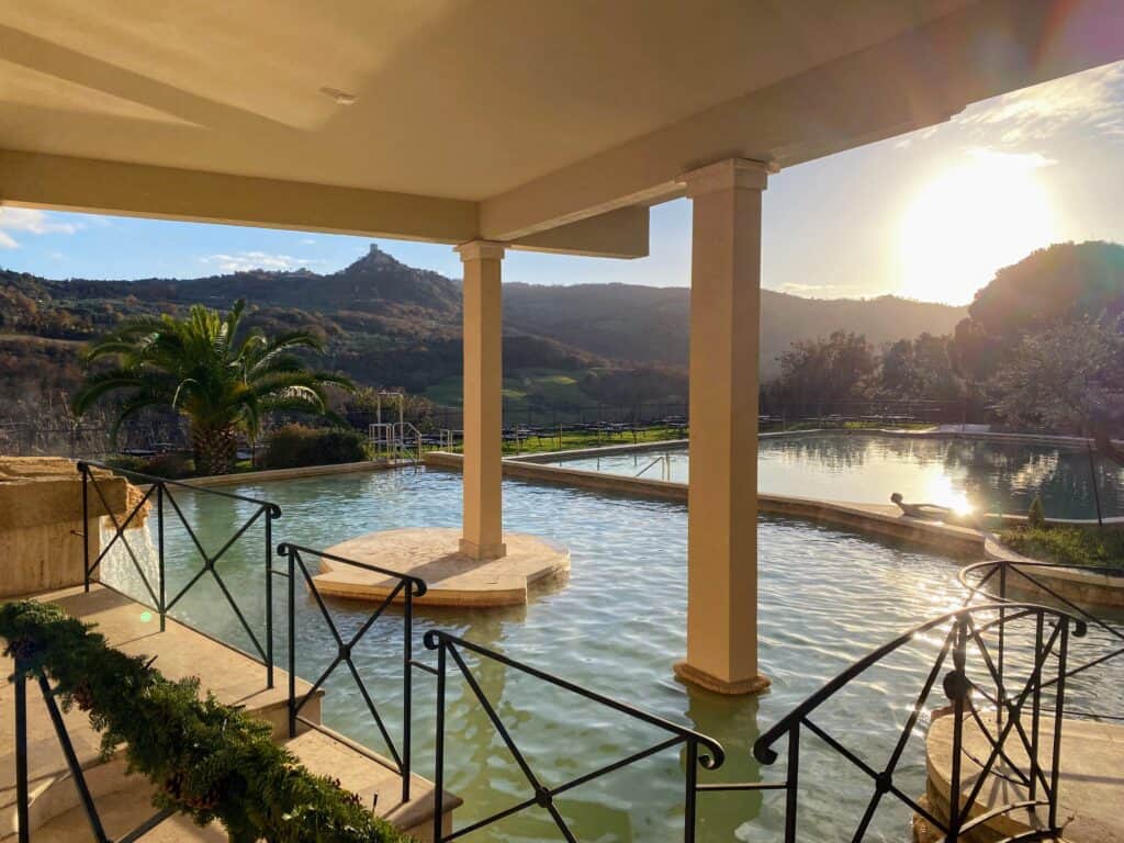 Outdoor thermal pool at sunset. Tuscan countryside in background.