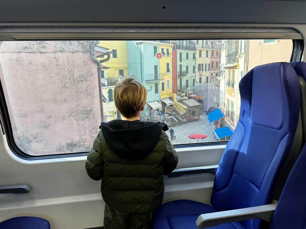 Boy stands at window on bus looking out at Cinque Terre village.