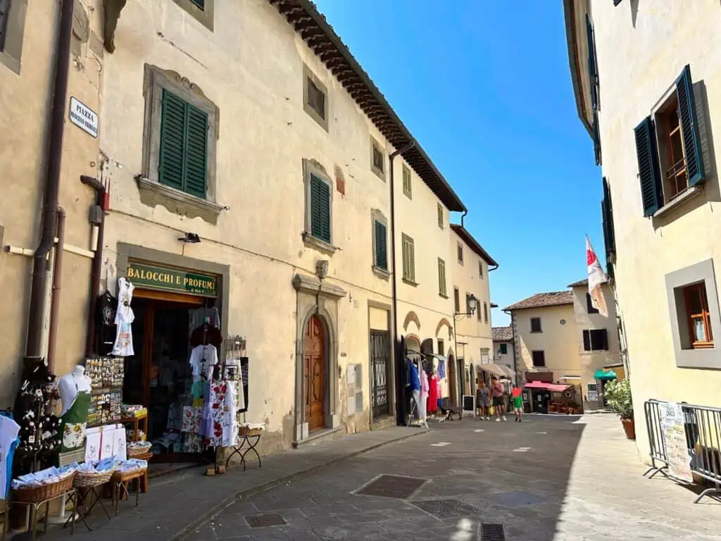 Narrow pedestrian street of Radda in Chianti with shops on left side and family walking at end of street.