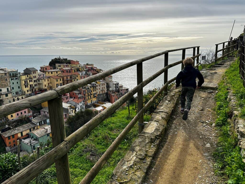 Boy runs on trail above the colorful village of Manarola on the left.
