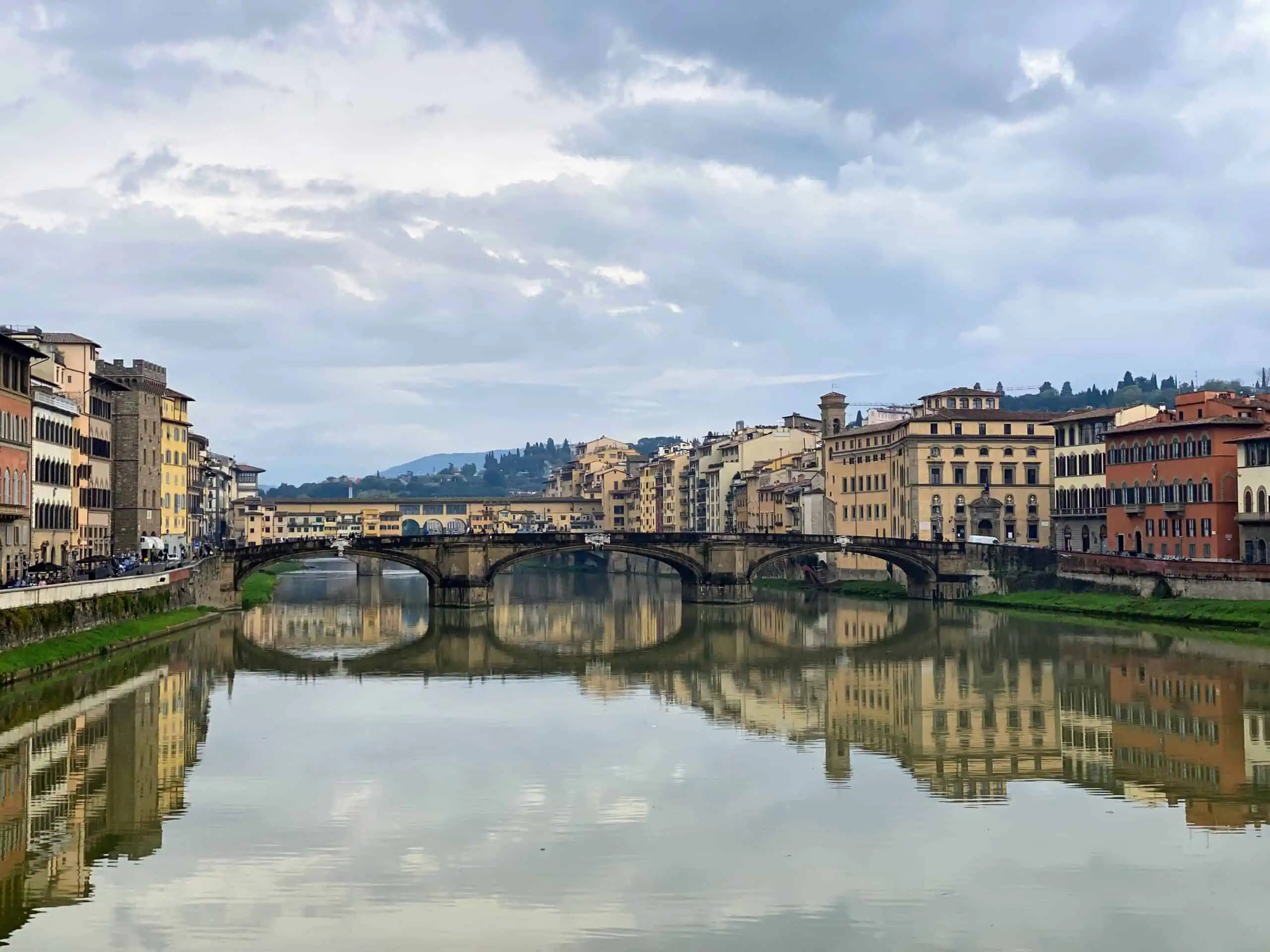 White clouds fill the sky above the Ponte Vecchio, which reflects onto the Arno River in Florence, Italy.