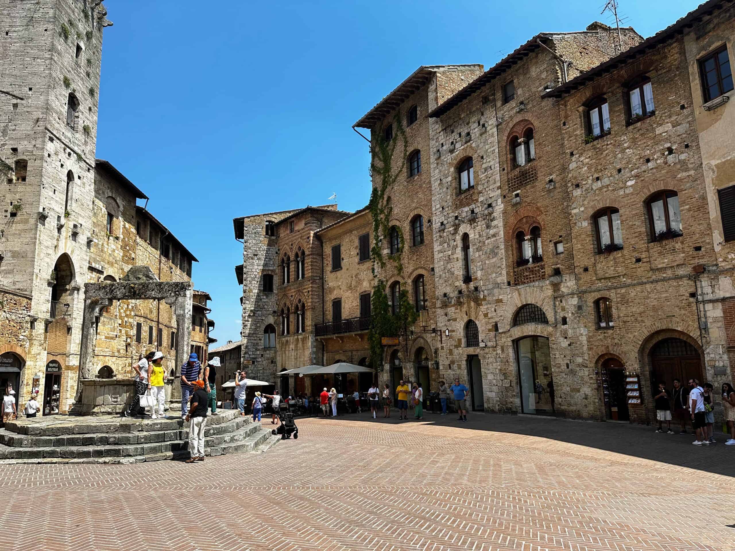 Italian piazza with stone buildings and a fountain. This is in San Gimignano, Tuscany, Italy.