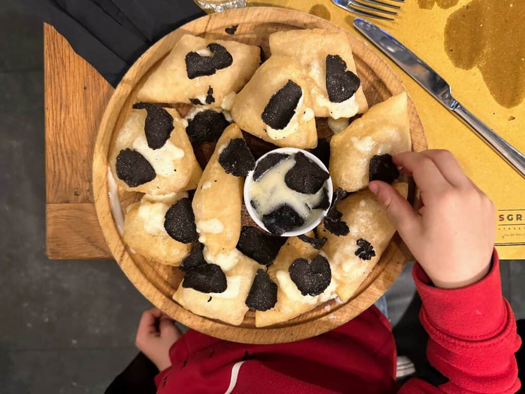 Child's hand reaches for a wooden plate of coccoli at Osteria Sgrano in Florence, Italy.