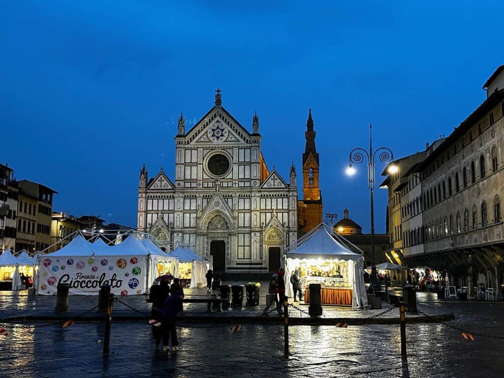 Piazza Santa Croce in Florence, Italy with tents set up for a chocolate festival. The church is in the background. It's twilight.