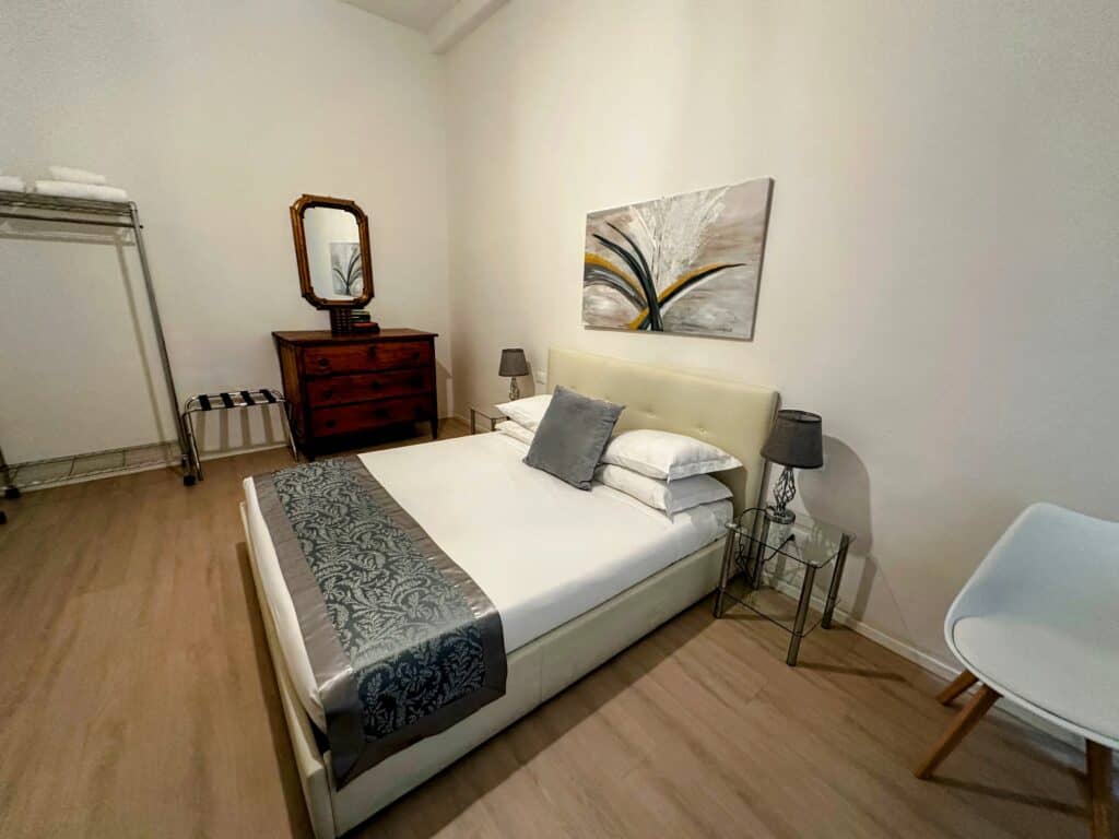 Bedroom in an apartment in Florence, Italy with bed, chair, side tables, and wooden dresser with mirror.