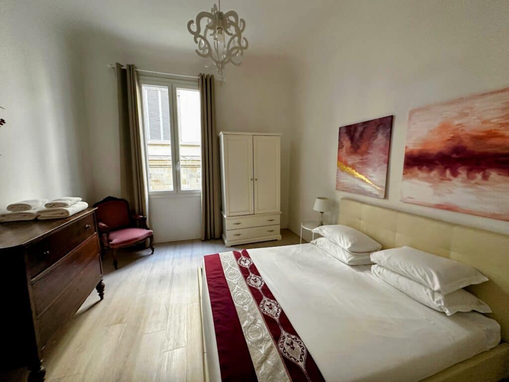 Bedroom in an apartment in Florence, Italy. The colors are red, white, and cream. There is a window on the back wall.
