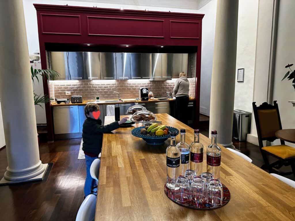 Boy reaches for croissant on display on a wooden table in the large kitchen at Peruzzi Residences in Florence, Italy. Woman in back prepares food at the sink.
