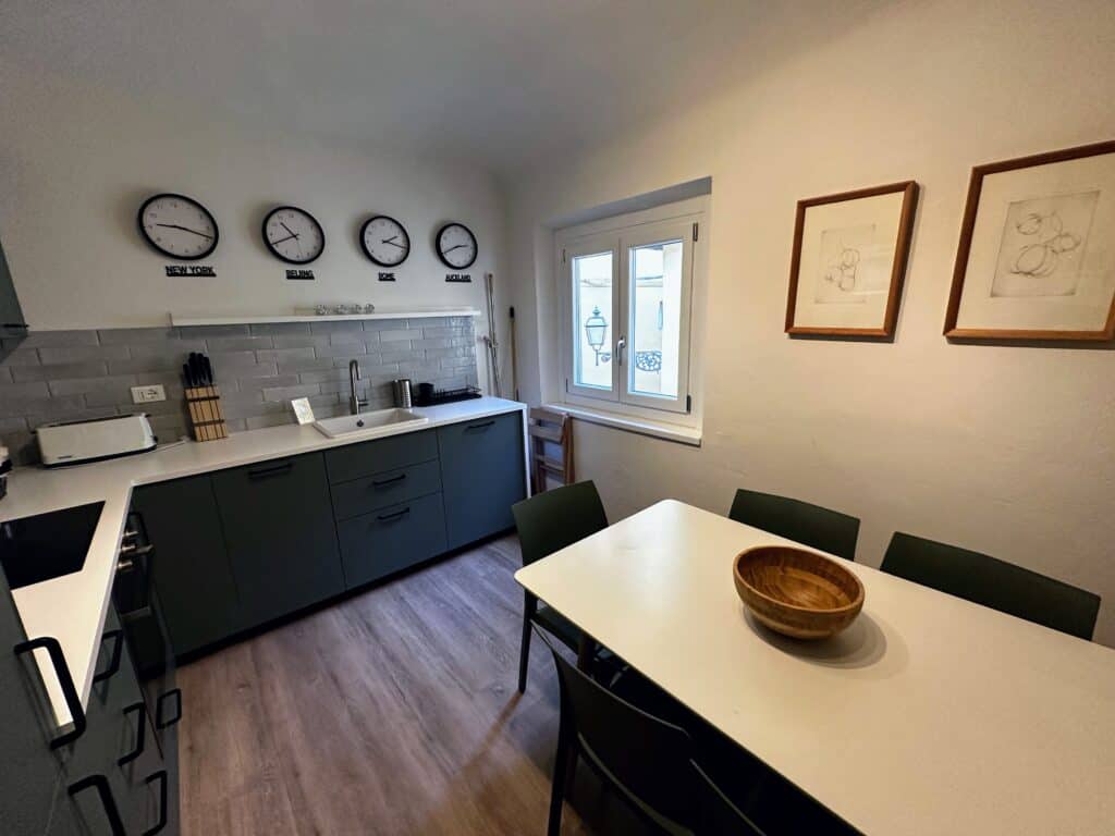 Kitchen in apartment in Florence, Italy. Four clocks on back wall, window on right, dining table on right.
