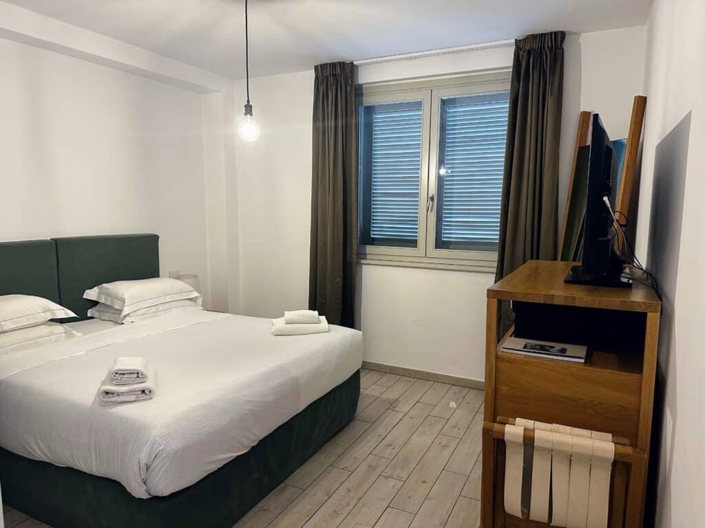 Bedroom in apartment in Florence with bed window, and tv on wooden dresser.