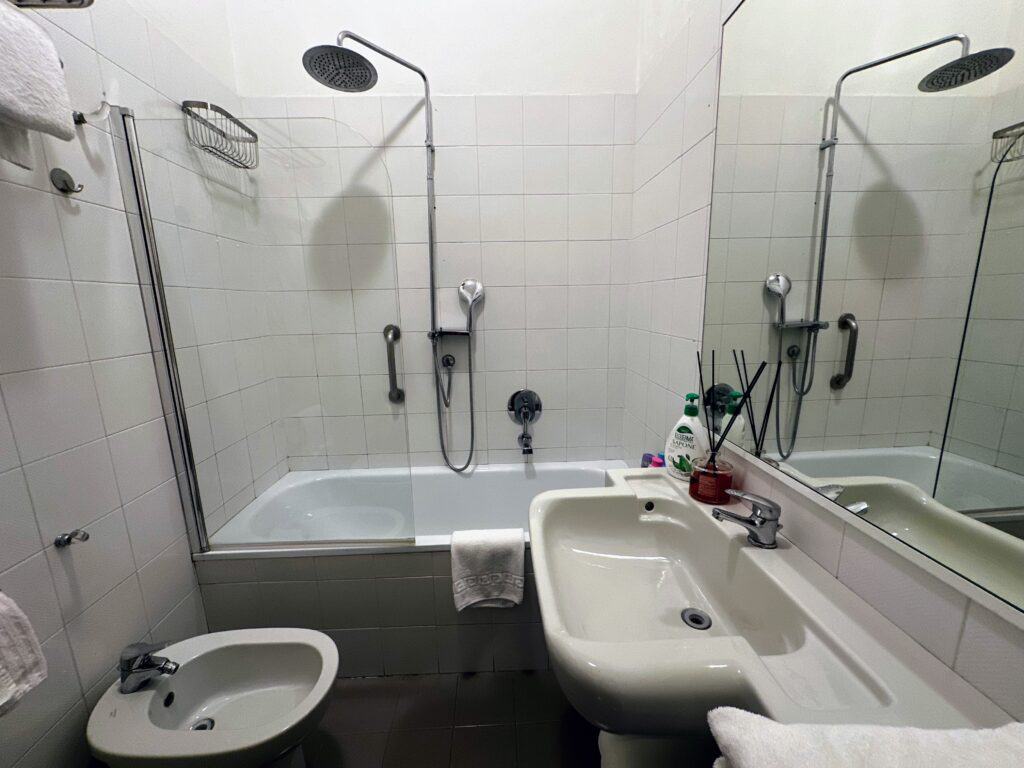 Bathroom in an apartment in Florence with white tiles, bathtub, shower, sink, and bidet.