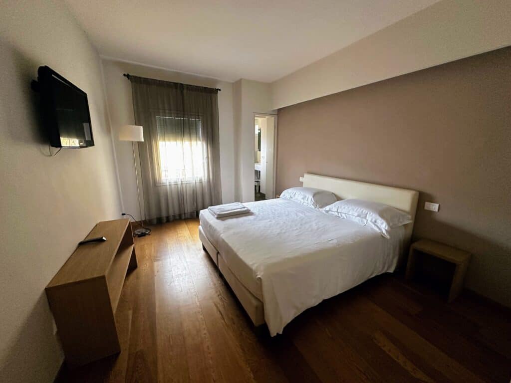Bedroom inside an apartment in Florence, Italy. Queen bed on right, tv on left, window in back of room along with door leading to bathroom.