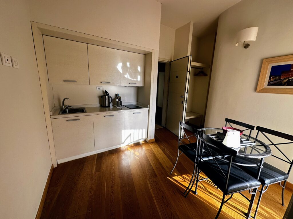Kitchen in apartment in Florence with wooden floor, beige cabinets, glass table, and black chairs.