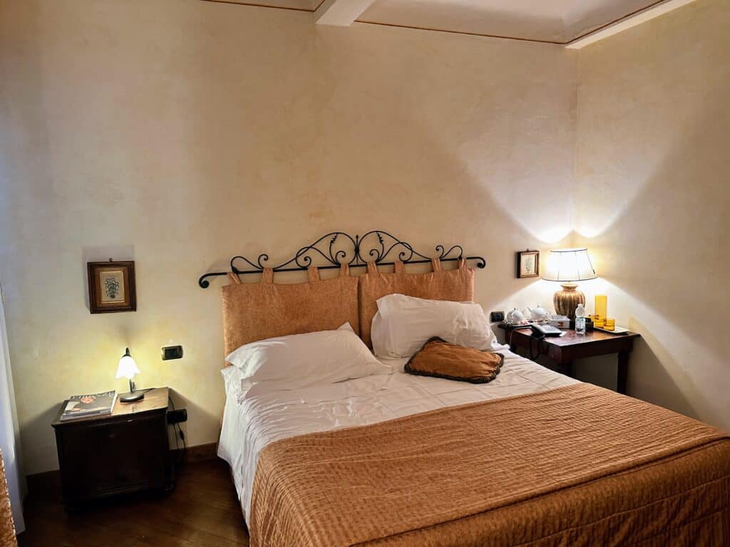 Bedroom with iron bed and peach covered bedspread in a hotel in Piazza della Signoria in Florence, Italy.