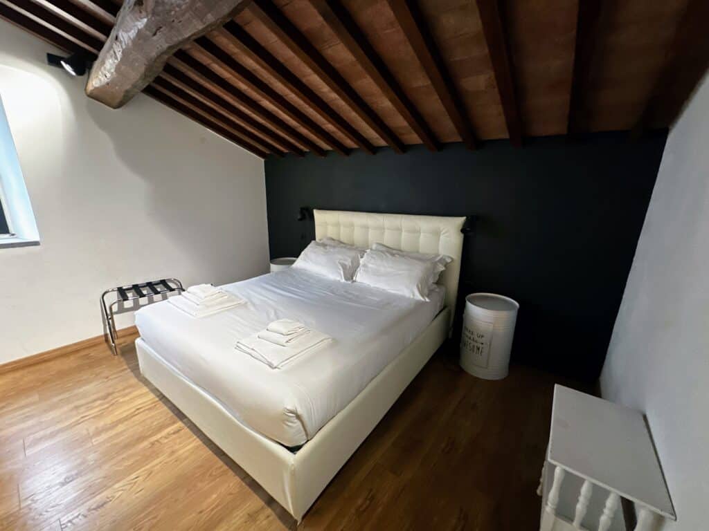 Bedroom in apartment in Florence, Italy with white bed against black wall. Wooden beams in ceiling. Wooden floor.