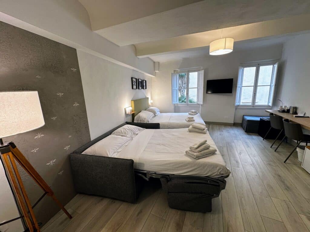 Sofa bed and queen bed in family room in Florence, Italy. Desk and chairs on right, windows in back.