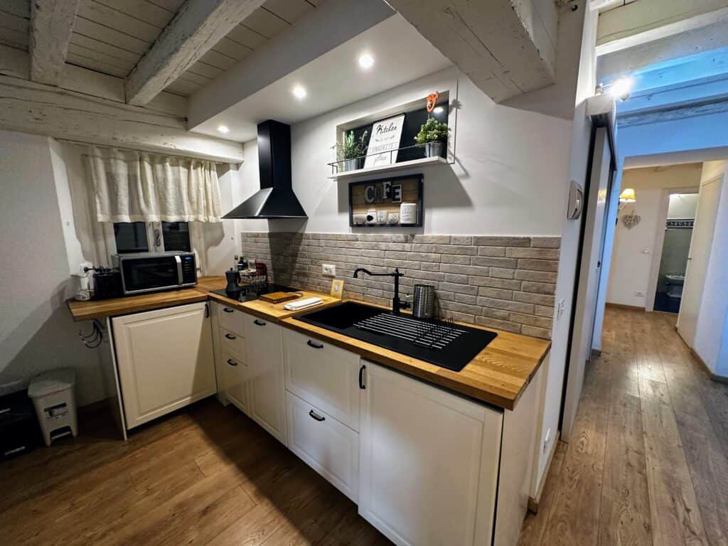 Kitchen in apartment in Florence, Italy. Counter space with sink, microwave, and stove. Hallway on left leads to other rooms.