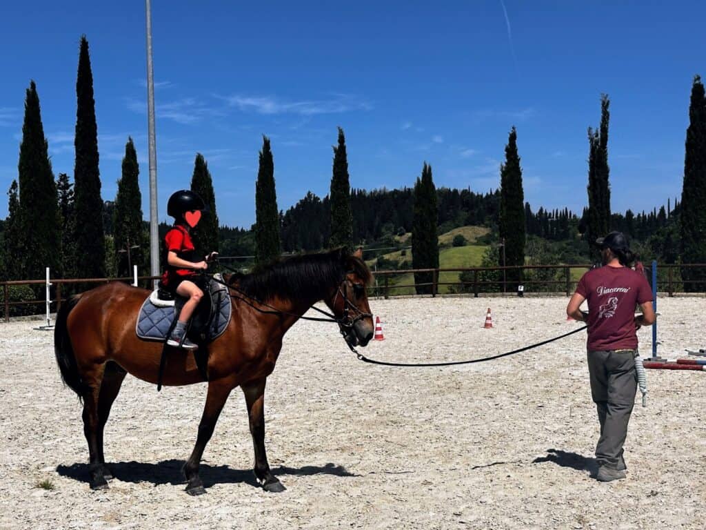 Boy rides a horse led by an instructor at the stables at Agriturismo Diacceroni in Tuscany, Italy.