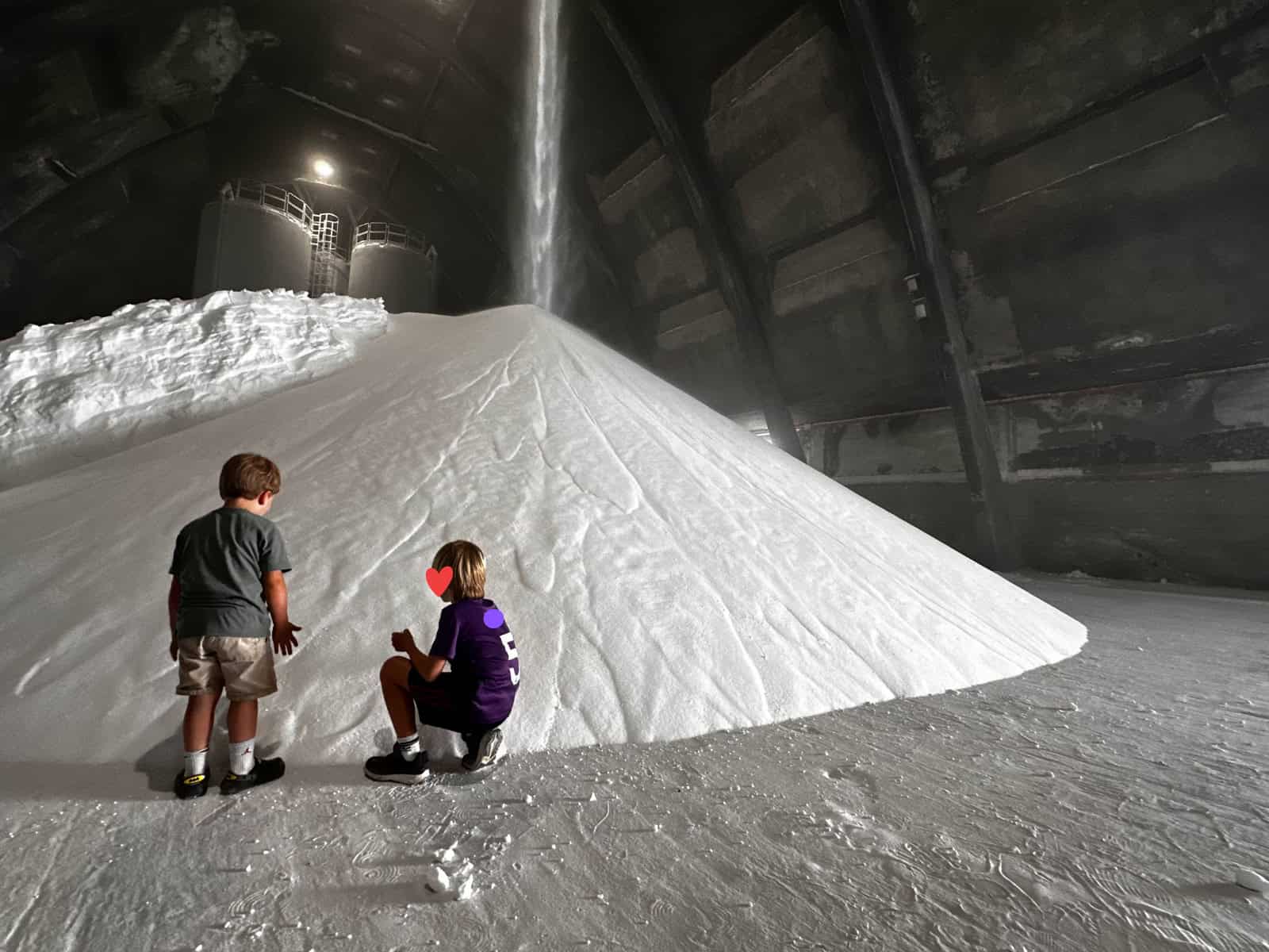 Boys stand at edge of large pile of salt at the Saline di Volterra in Tuscany, Italy.