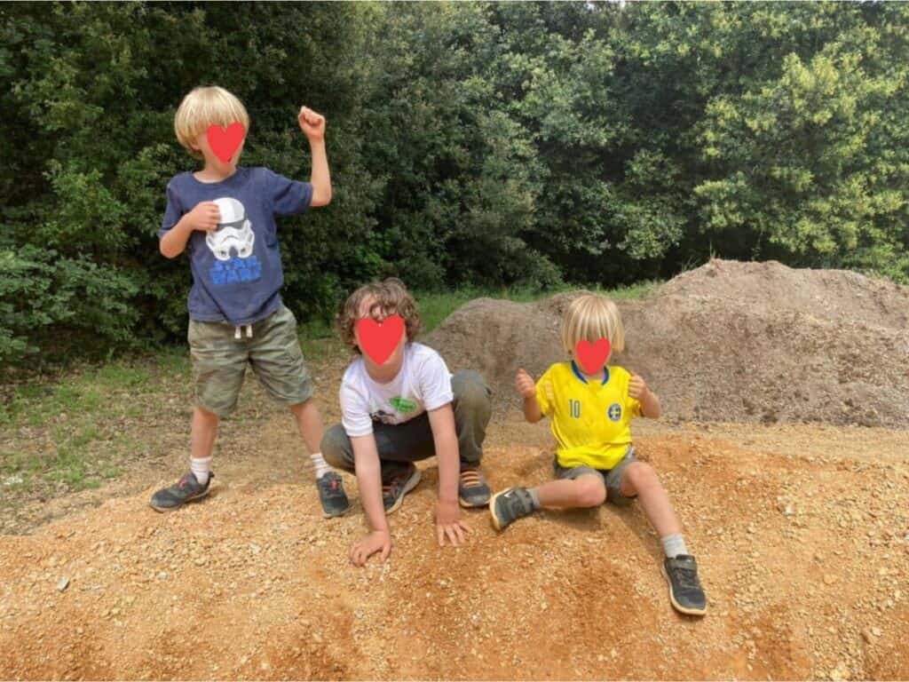 Three boys sitting/standing on a dirt pile in Tuscany.