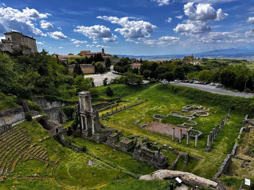 View of grassy ruins of Roman theatre in Volterra, Italy, as seen from above.