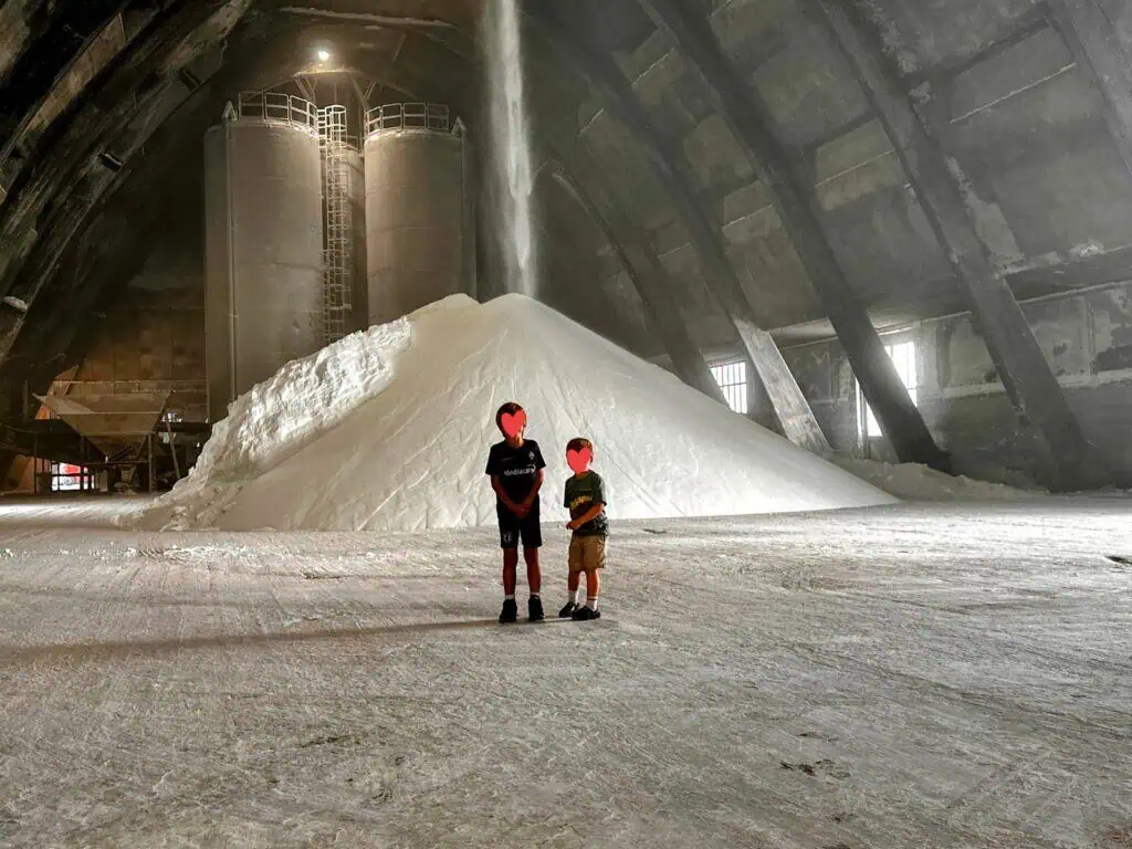 Two boys stand in front of a large mountain of salt and salt pouring onto it from the ceiling.