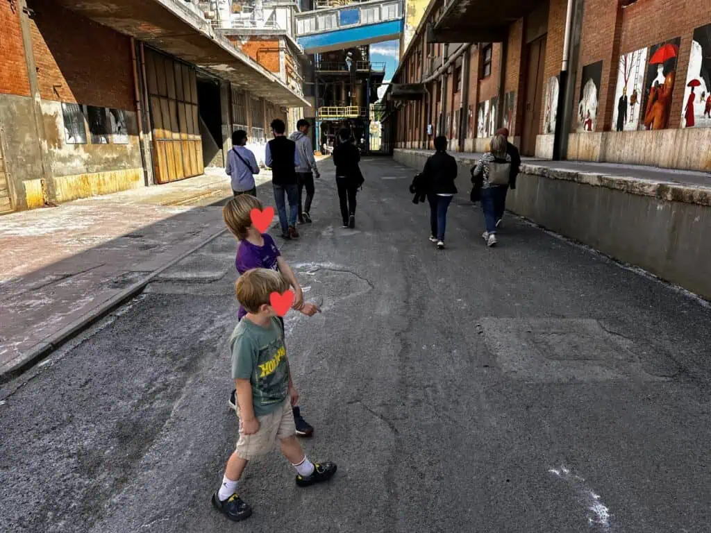Boys and tour group walk outdoors, between buildings at the Volterra Salt Works in Tuscany.