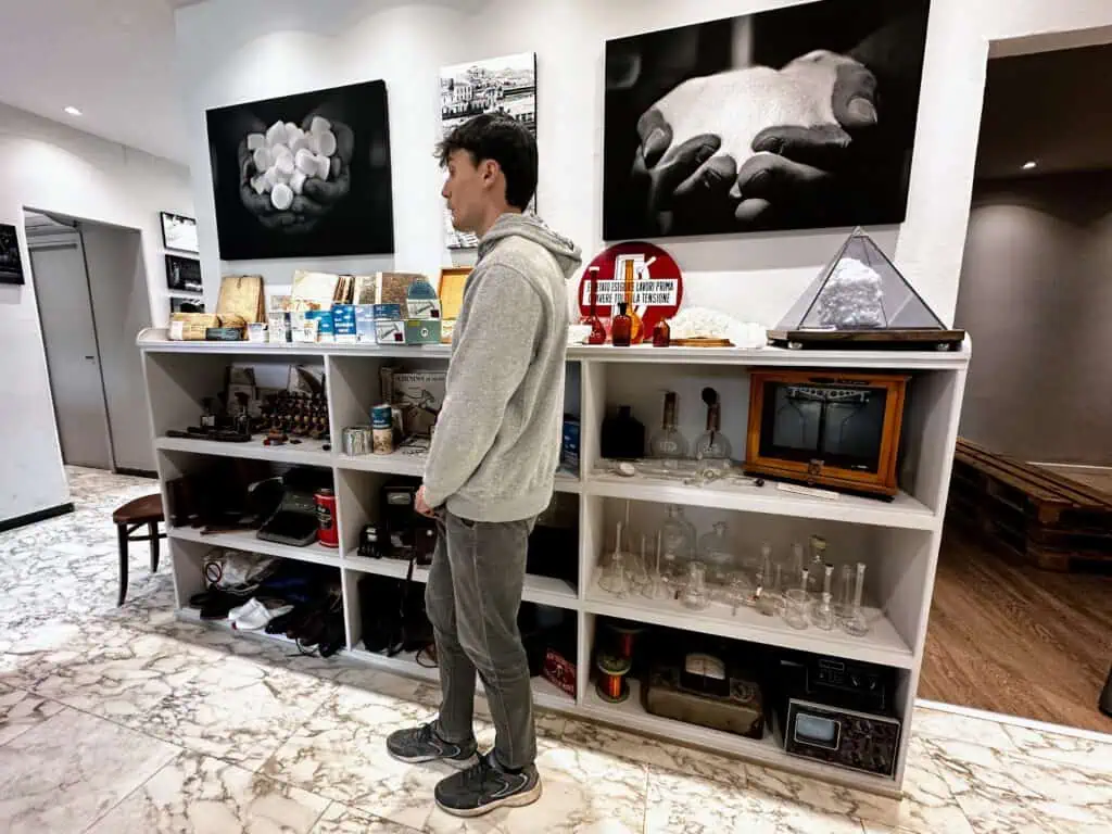 Guide stands in front of artifacts on shelves and handing on the wall at the Volterra Saltworks Museum in Tuscany.