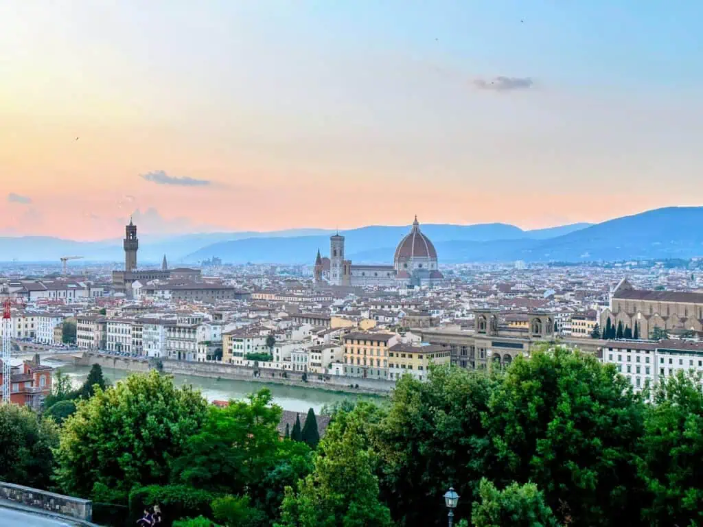 Florence, Italy skyline at dusk on a May evening. Duomo and Giotto's bell tower and Palazzo Vecchio stand out. Lush, green trees in the foreground.
