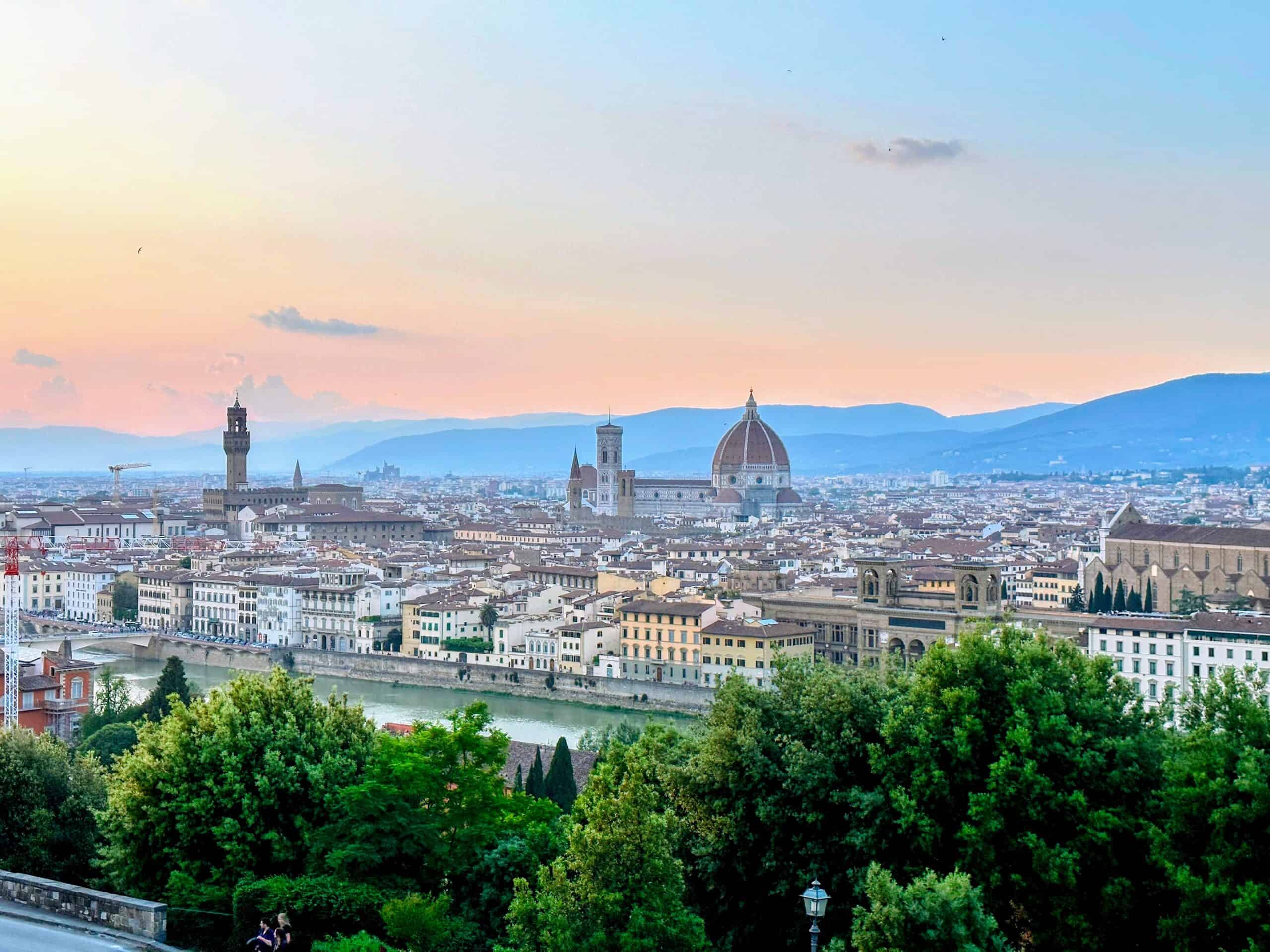 Florence, Italy skyline at dusk on a May evening. Duomo and Giotto's bell tower and Palazzo Vecchio stand out. Lush, green trees in the foreground.