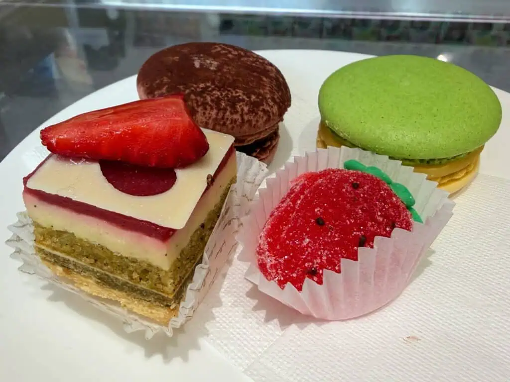 Small plate with paper napkin and strawberry gelee, two macarons, and and a layered strawberry cake.