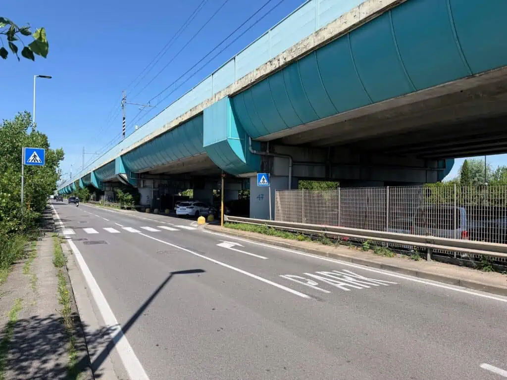 PARK and an arrow that points right on the pavement of a road that's parallel to an overpass or train line. A few cars on the road ahead and one car has just turned toward the arrow to go under the overpass.