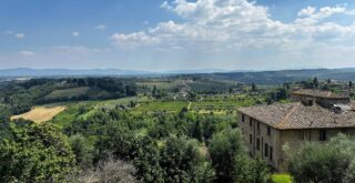 Green countryside of Tuscany on a sunny day with puffy white clouds. Stone building on right in foreground.